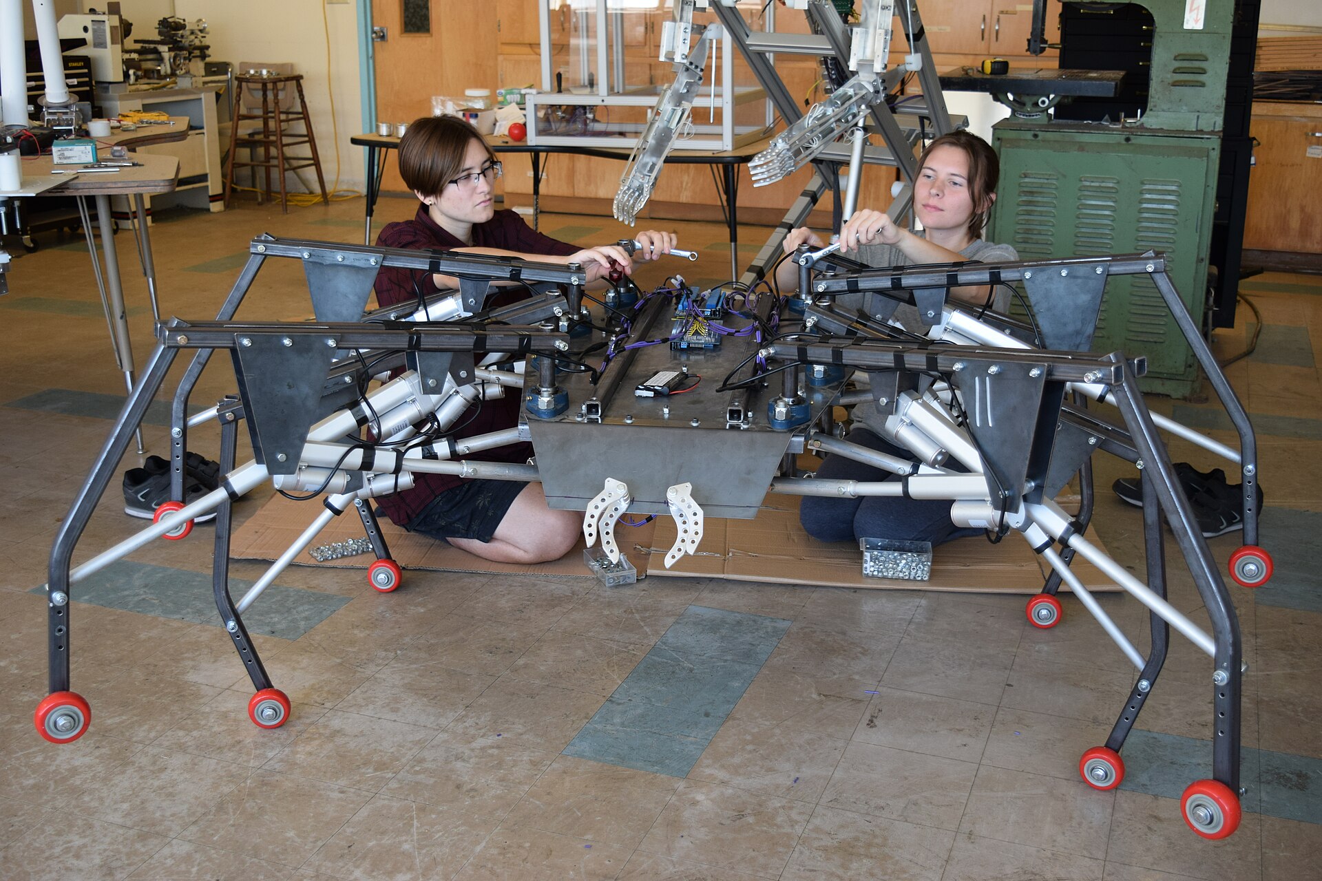 Sisters Aurora and Autumn Siegel, the youngest members of the MRISAR R&amp;D team, began their apprenticeship in Robotics as preschoolers. They are seen here helping to complete a hand crafted 7’ wide, giant interactive, mobile robotic spider between other workshop robotics projects and machine shop equipment. This bio-inspired robotic spider is a device created for public use in museum environments to help educate millions of people worldwide and is a good example of bio-mimicry. The Robotic spider was designed by MRISAR’s R&amp;D team and fabricated at MRISAR, a family owned business in North Dakota. The team goals are humanitarian and educational uses for science, art &amp; technology. The devices created at the labs and workshops are unique in the fact that they are handcrafted, not mass produced. This allows the creative team to create across a wide range of technologies, applications and elements of science and art. Everything from MRISAR is designed and prototyped by two generations of 4 family members, the youngest two Autumn and Aurora Siegel, along with their parents John Siegel and Victoria Lee Croasdell-Siegel. The public use robotic exhibits they create for museums and science centers around the world relate to STEM and STEAM. This two generation team has even invented robotic systems for NASA. Science in combination with art relate to a better understanding of engineering and technology which can be used to develop devices that enrich education and save lives. Creating handcrafted elements of engineering based on bio-inspired elements and abstract reasoning is a way to use the creation of such devices to explore how nature develops engineered creative aspects that humanity can use. Such devices can serve as valuable elements of education and research to be used to develop devices that can save people from disasters, preform special industrial tasks and in other unique uses. From a technical vantage this specific device combines electromechanical and mechanical engineered elements with travel limits and Boolean logic to achieve a goal of creating systems that can instantly adapt to their surroundings. Other key elements are observations of design standards such as compensation for mechanical shock load, derating electrical, derating mechanical, derating electronic and mechanical elements, analysis of materials, weight distribution and comparisons to human arm operating degrees of freedom. Great care must be taken in design, development and testing. Just one error in design or logic parameters and a device that weighs hundreds of pounds, and made with thousands of parts can come dramatically crashing to the ground. Preliminary tests are therefore done while the device is fully supported on pedestals or with support lines. More images of the creation of this and other MRISAR robotic devices can be seen at mrisar.org. The work of MRISAR’s R&amp;D team has drawn world interest for their public-use educational robotic exhibits prototypes and also for their humanitarian R&amp;D that aims to improve the quality of life. Their work has been presented before and/or published and awarded by: the United Nations, NASA-Emhart, Stanford, Cambridge, ICORR Robotics conferences, ROMAN Robotics conferences, IEEE, Discover Awards, International Federation of Robotics, etc. The “International Federation of Robotics” annual publication on Service Robotics regularly lists MRISAR Institute of Science, Art &amp; Robotics in at least ten categories of robotics. The publication covers major contributors in the field of robotics and within that coverage focuses on the diversity of robotics, worldwide uses for robotics, economic factors and projections. Most are industrial providers, but the publication also includes NASA and other renowned research elements that reach well beyond industrial applications. In the 2011 publication MRISAR was featured in an entire chapter. The publication picks one per year for special focus in a chapter and covers a multitude of ventures in the rest of the document.